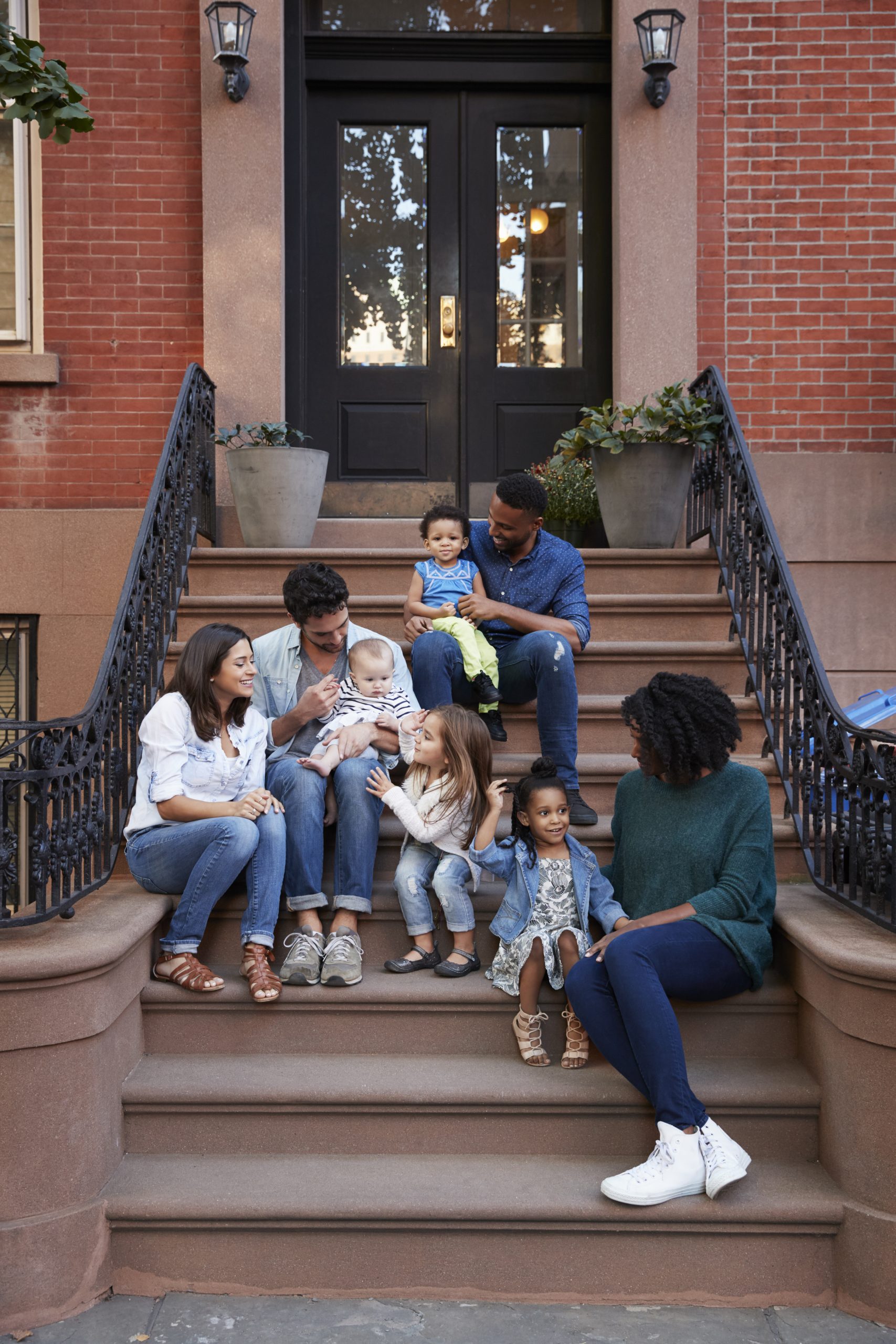 Two families with kids sitting on front stoops, vertical